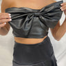 Frontal view of the My Muse Crop Top that features a black PU material, a sleeveless design with a straight neckline, a bow detail at the bust, a smocked back, and a cropped fit.
