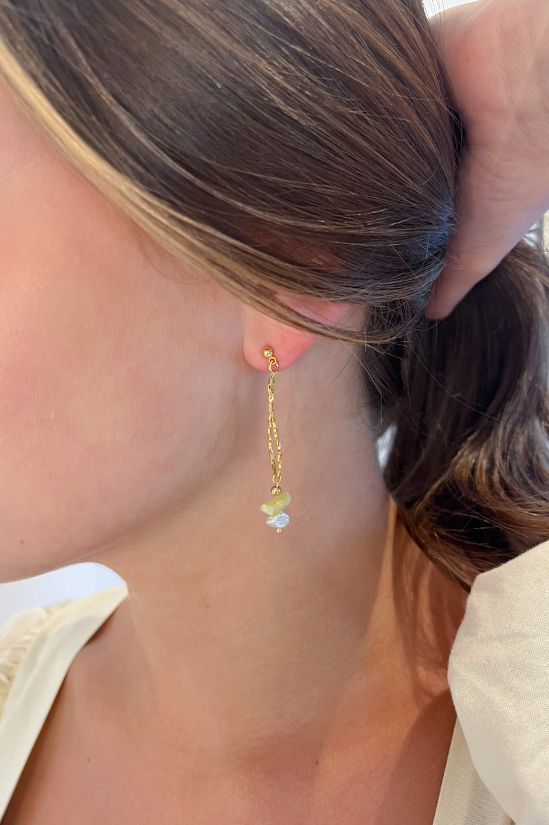 Close side view of model wearing the Summer Fling Earrings that have a hammered gold tear drop shape with a white and yellow bead.