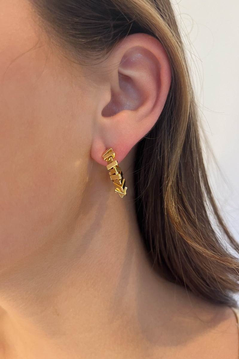 Side view of model wearing the Out Of Line Hoops which features open, small hoops covered with gold bars design.