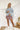 Frontal view of the Born Lucky Denim Jacket that features a light washed denim material, a collard neck, mild distressing, fading, front flap, two front pockets, a frayed hem, V cut open back with beaded fringe detailing