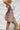 Side view of the Out On The Town Skort that features a mauve colored material, a high-rise fit, a thick elastic waist band with a ruffle detail, a ruffled tiered design, a shorts lining, and a mini length.