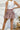Back view of the Out On The Town Skort that features a mauve colored material, a high-rise fit, a thick elastic waist band with a ruffle detail, a ruffled tiered design, a shorts lining, and a mini length.