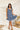 Frontal view of the Cross Roads Dress that features a blue and white floral pattern, a straight neckline, a sleeveless design with a thick ruffle strap, a tiered design, and a flowy fit.