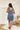 Back view of the Cross Roads Dress that features a blue and white floral pattern, a straight neckline, a sleeveless design with a thick ruffle strap, a tiered design, and a flowy fit.