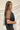 Side view of the Mirror Mirror Top that features a black sheer fabric, a rounded neckline with a sheer lining at the chest, a sheer puffy half sleeve, a flowy fit, and a button back.