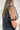 Side view of the Mirror Mirror Top that features a black sheer fabric, a rounded neckline with a sheer lining at the chest, a sheer puffy half sleeve, a flowy fit, and a button back.