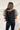Back view of the Mirror Mirror Top that features a black sheer fabric, a rounded neckline with a sheer lining at the chest, a sheer puffy half sleeve, a flowy fit, and a button back.