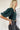 Side view of the Turn Back Time Top that features a green corduroy material, a straight neckline, a half puffy sleeve, a smocked back, and a cropped fit.