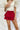 Frontal view of the Maeve Skort that features a red satin material, a thick elastic waist band with a tie detail, a ruffle tiered design, a shorts lining, and a mini length.