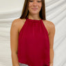 Frontal view of the Unwritten Tank Top that features a red material, a halter neck, a sleeveless design, a pointed front and back, and a flowy fit.