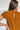 Back view of the Hampton Social Top that features a caramel material, a high rounded neckline with a ruffle hem, a short flowy sleeve, a pleated design, a lettuce edge bottom hem, and a flowy fit.