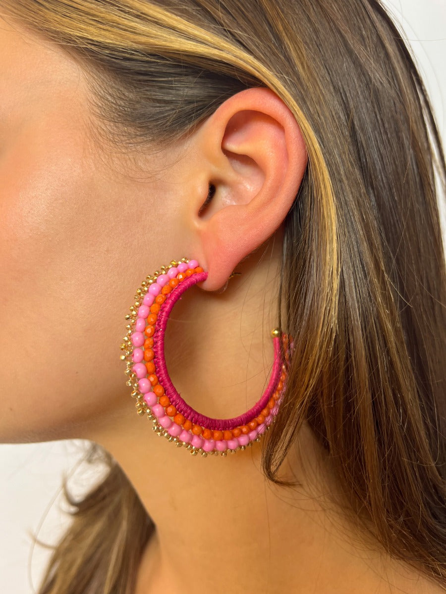 Side view of model wearing the Full of Life Earrings which features open, large size hoop with orange, hot pink, light pink and gold beads.