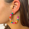 Side view of model wearing the Dream On Earrings in Multi which features medium, closed hoop covered with teal, fuchsia, light pink, orange and marigold beads.
