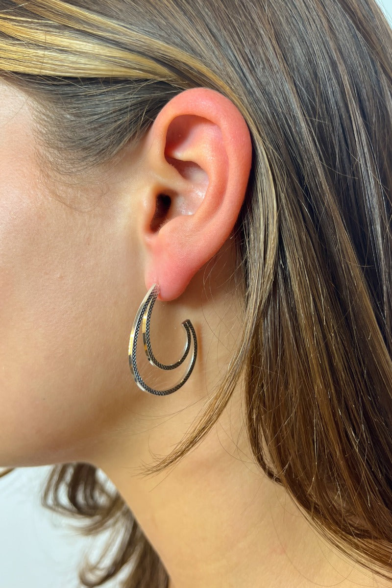 Side view of model wearing the Small Things Earrings in Silver which features medium, open scooped hoops with silver textured and two-layered design.
