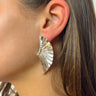 Side view of model wearing the Fly Away Earrings in Silver which features silver wing-shaped earrings with a pleated design.