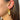 Side view of model wearing the Fly Away Earrings in Gold which features gold wing-shaped earrings with a pleated design.