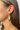 Side view of model wearing the Fly Away Earrings in Gold which features gold wing-shaped earrings with a pleated design.