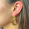 Side view of model wearing the Link Up Earrings which features gold dimensional shaped hoops linked together.