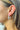 Side view of model wearing the Star Gazing Earrings in White which features small open white hoop with red and blue stars design outlined in gold details.