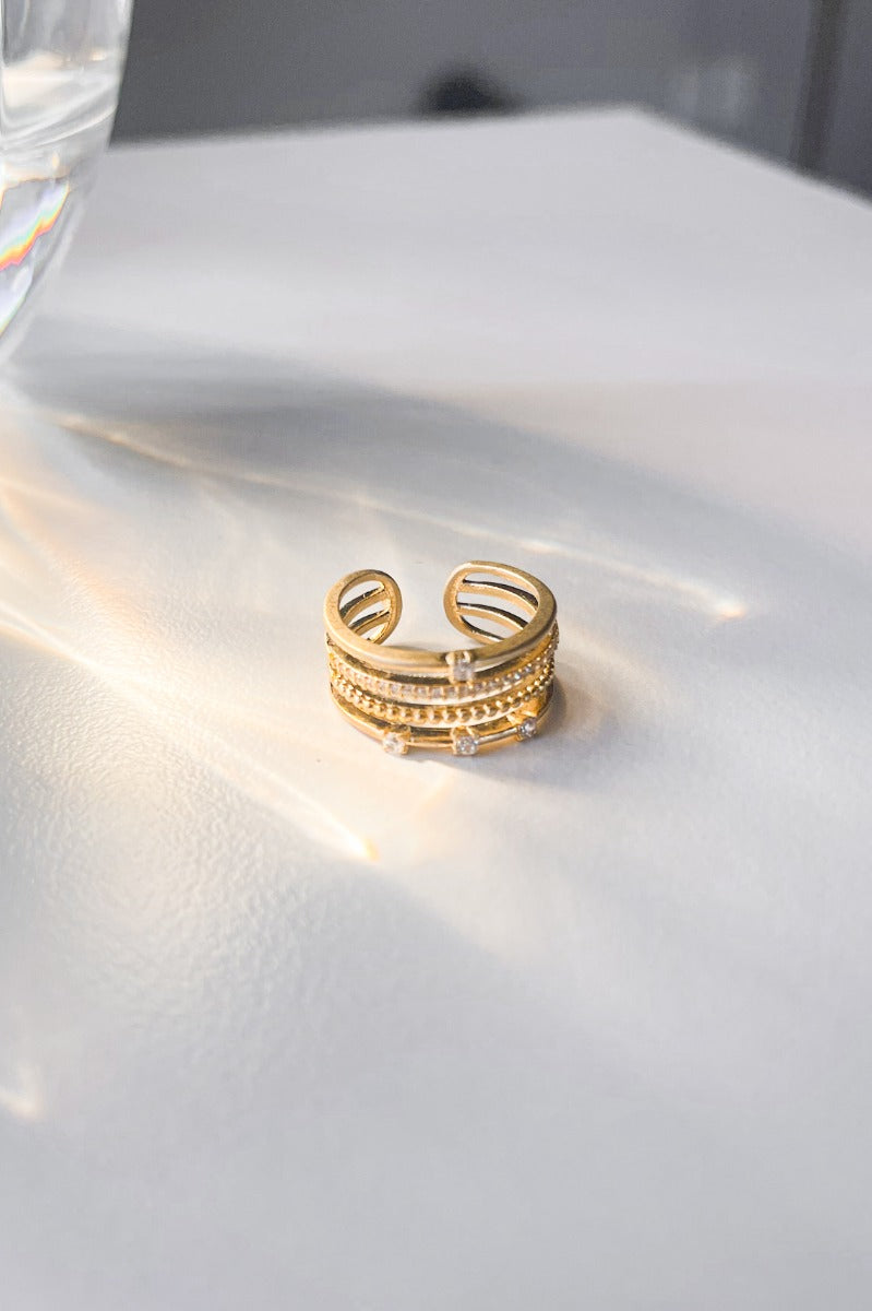 Flat lay of the Fantasy Dreams Ring which features dainty four gold bands, one band with three clear stones, one band with one clear stone and one band with multi clear stones.