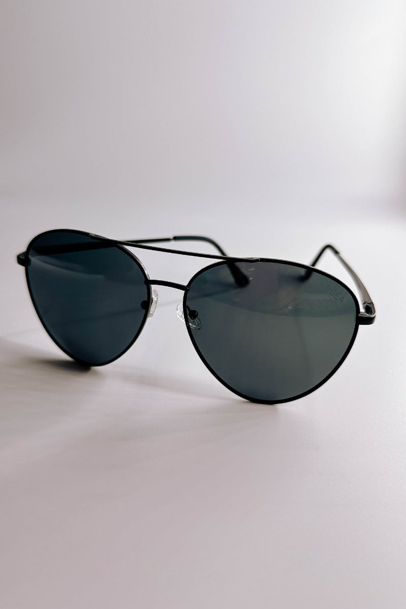 Front view of model wearing the I-Sea: Charlie Sunglasses in Black which features aviator shaped black frames and black lenses. 