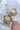 The Oh Honey Earring is a dangle style earring featuring a honey comb design with a gold outlined bee with a white fill color.