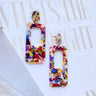 The Mid-Century Earring is a dangle style earring featuring a multi-colored design.