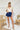 Frontal view of the Maeve Skort that features a blue satin material, a thick elastic waist band with a tie detail, a ruffle tiered design, a shorts lining, and a mini length.