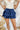 Frontal view of the Maeve Skort that features a blue satin material, a thick elastic waist band with a tie detail, a ruffle tiered design, a shorts lining, and a mini length.