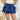 Frontal view of the Maeve Skort that features a blue satin material, a thick elastic waist band with a tie detail, a ruffle tiered design, a shorts lining, and a mini length.