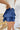 Side view of the Maeve Skort that features a blue satin material, a thick elastic waist band with a tie detail, a ruffle tiered design, a shorts lining, and a mini length.