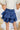 Back view of the Maeve Skort that features a blue satin material, a thick elastic waist band with a tie detail, a ruffle tiered design, a shorts lining, and a mini length.