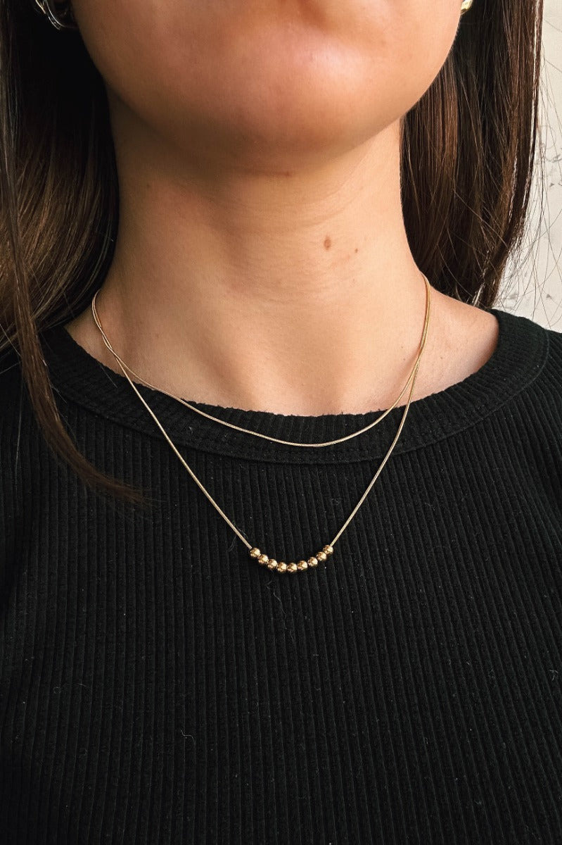 Close up view of model wearing the Ellie Gold Layered Bead Necklace which features double gold layer with gold bead details.