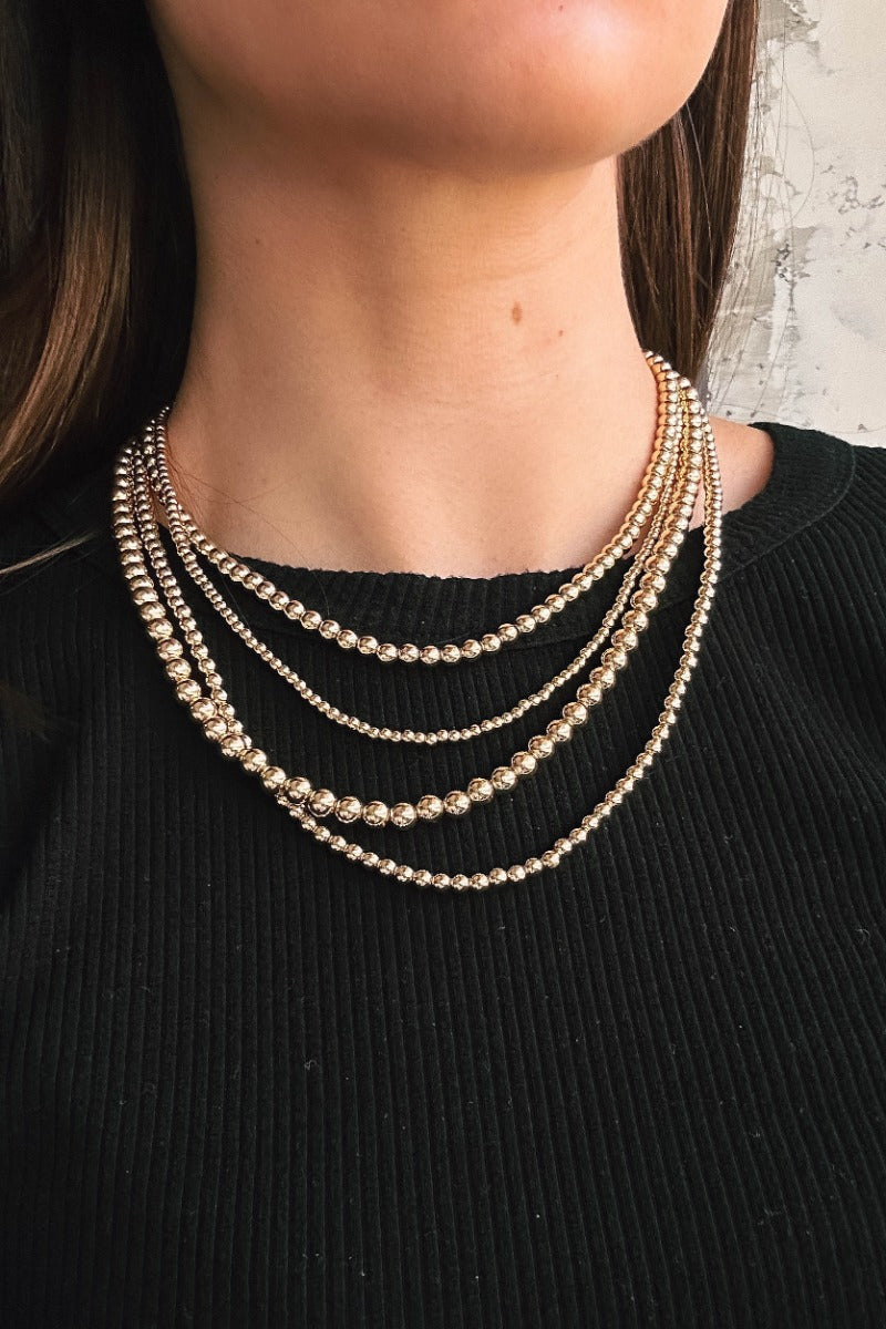 Close up view of model wearing the Emma Gold Beads Layered Necklace which features four layers of small and medium gold beads with adjustable clasp closure.