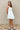 Full body view of model wearing the Prepare To Swoon Dress which features white fabric, mini length, white lining, pockets on each side, boning upper details, square neckline, thick straps, sleeveless and monochromatic back zipper with hook closure.