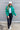 Full body front view of model wearing the Call It Even Puffer Jacket features green puffer fabric, two front pockets, a high neckline, a silver zip up, and long sleeves