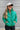 Close up view of model wearing the Call It Even Puffer Jacket features green puffer fabric, two front pockets, a high neckline, a silver zip up, and long sleeves