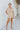 Frontal view of the Runaway Summer Romper that features a V neckline, a short cuffed sleeve, a ruched front, a cinched waist band, and a cuffed bottom hem.