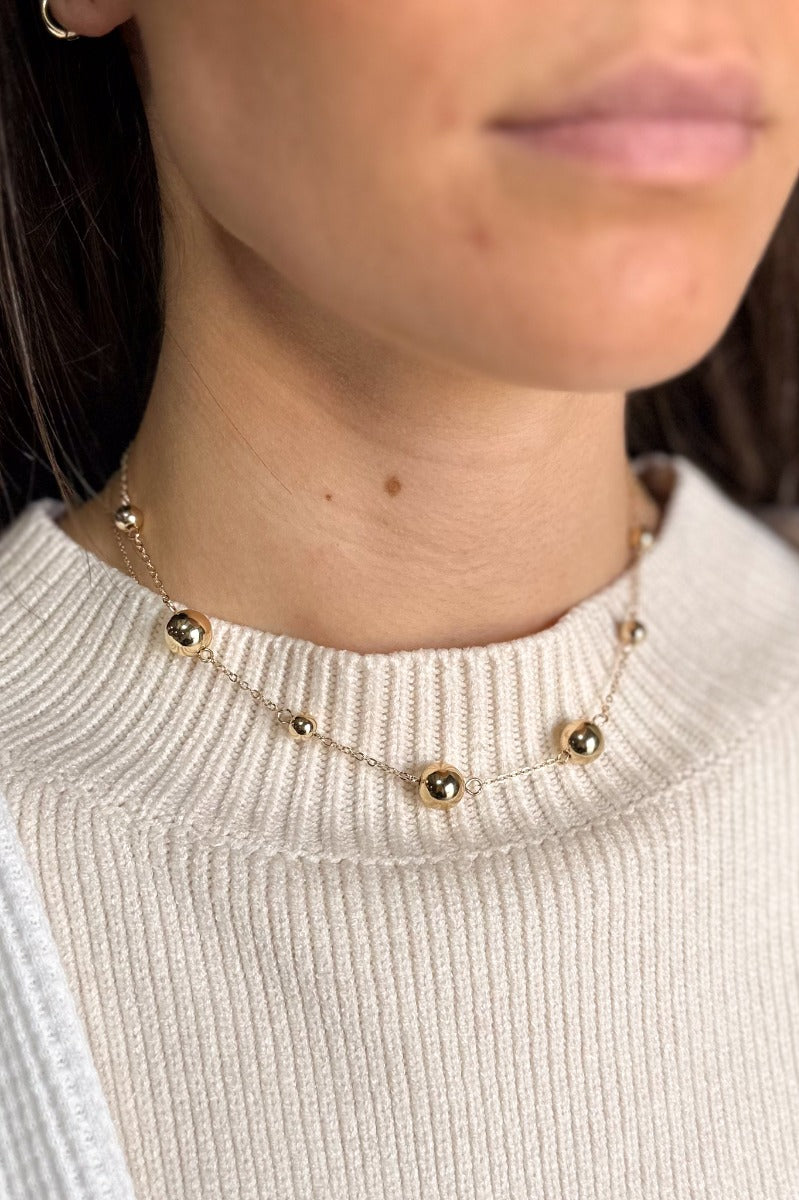 Front view of model wearing the Baker Gold Bead Chain Necklace which features single gold chain link with small and medium gold beads.