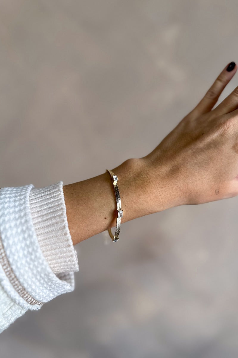 Front view of model wearing the Taylor Clear Stones & Gold Flat Bracelet which features gold flat band with three rectangle clear stones and adjustable closure.