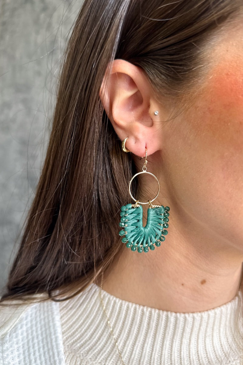 Front view of model wearing the Natalie Dark Green Knit & Gold Dangle Earring which features gold dangle hoops linked with a scooped hoop, dark green yarn details and dark green beads.