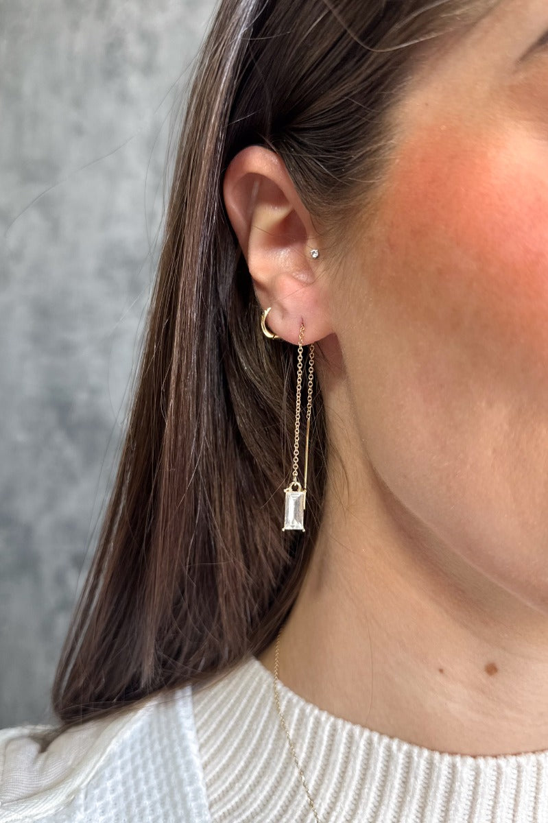 Side view of model wearing the Deena Gold Chain Rhinestone Dangle Earring which features gold dangle earrings linked to clear rectangle shaped stones.