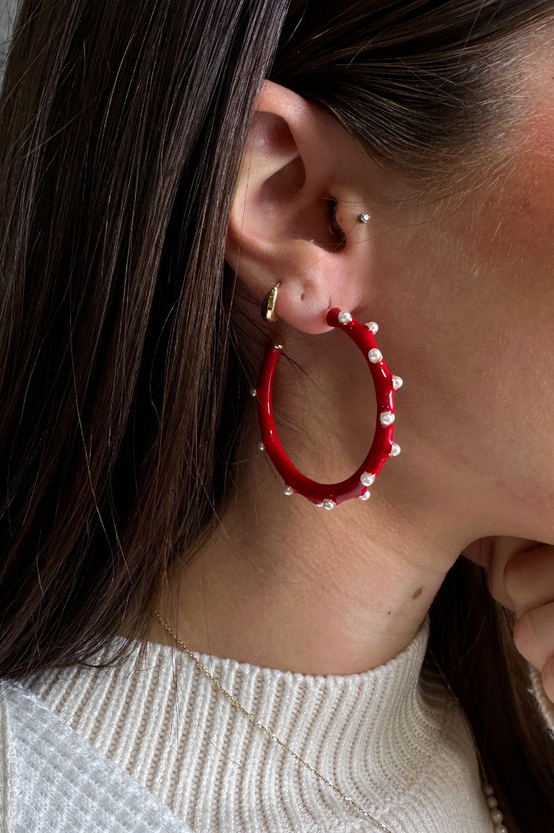 Close up view o fmodel wearing the Patricia Pearl Red Hoop which features medium red open hoops with mini pearl details.