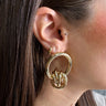 Front view of model wearing the Camryn Gold Intertwine Dangle Earring which features open gold circle linked with an intertwined gold ball. 