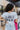 Close up back view of model wearing the King Of Rock Cropped Graphic Tee which features white fabric with a distressed cropped waist, short sleeve and a round neckline. The front has in image of Elvis Presley with "Elvis Presley" in pink text. The back im