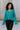 Close up front view of model wearing the Spin Me Around Sweater which features green ribbed loose-knit fabric with monochromatic confetti, white trim on the shoulders, a notched neckline, and long sleeves.