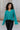 Close up front view of model wearing the Spin Me Around Sweater which features green ribbed loose-knit fabric with monochromatic confetti, white trim on the shoulders, a notched neckline, and long sleeves.