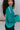 Close up side view of model wearing the Spin Me Around Sweater which features green ribbed loose-knit fabric with monochromatic confetti, white trim on the shoulders, a notched neckline, and long sleeves.
