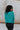 Back view of model wearing the Spin Me Around Sweater which features green ribbed loose-knit fabric with monochromatic confetti, white trim on the shoulders, a notched neckline, and long sleeves.