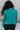 Close up back view of model wearing the Spin Me Around Sweater which features green ribbed loose-knit fabric with monochromatic confetti, white trim on the shoulders, a notched neckline, and long sleeves.